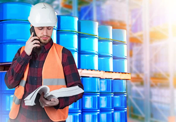 Oil. Man next to blue barrels. Oil barrels are stored in metal barrels. Man works at a petroleum product warehouse. Storage and transportation of gasoline. Guy is talking on phone. Sale of petroleum