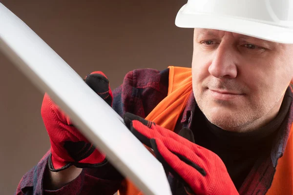 Builder shows a white board. Builder in holds sample in hands. Worker shows a white sheet. Concept - man is showing something. Satisfied. Human in a helmet of builder. Concept - demonstrates quality