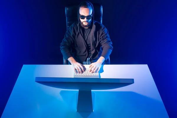 Blue background with a man at the computer. Symmetrical image of a person at a computer. A man in black clothes and glasses works on a PC.