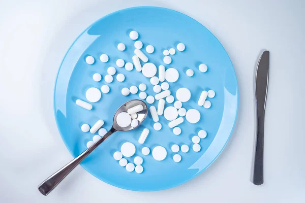 Pills on a plate next to the Cutlery. Many different tablets on the plate. Pharmacology. Use of a large number of medications. Self-treatment.