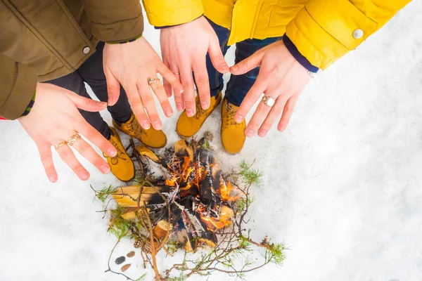 A man and a woman warm their hands by the fire. People stretch out their hands to the fire. Winter walk. A couple warms up by the fire in winter. Outdoor recreation. Stay in the fresh air.