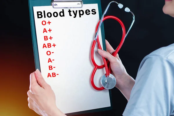 The doctor is holding a notebook with the names of blood groups and rhesus factors. Determination of blood group. Blood test result. Important medical information about the patient.
