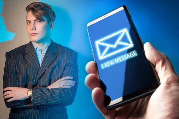 1 new message. Young man is holding out a telephone. Concept - person is shown a new message on the phone. Concept - transfer of SMS messages may be. Guy in a business suit. Man crossed his arms. One