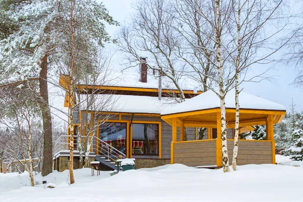 Winter holidays in cottages. Wooden house and gazebo on the background of snow. Cottage with panoramic Windows. Winter holidays away from the city. Cottage rentals. Stay in the fresh air.