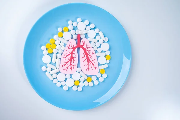 The concept of the treatment of lung diseases. Human lungs and pills on a blue plate. Fight against bronchial asthma. Medications for lung health.