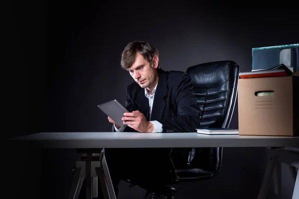Dismissal man. Fired man at office table. Workplace cardboard box as symbol of dismissal. Concept - dismissal are looking for work in internet. Young man with a tablet in his hands. Dismissed manager