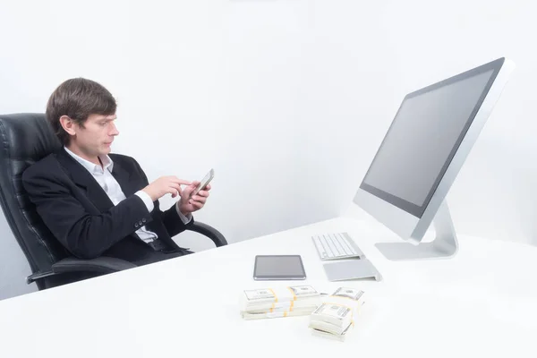 Portrait of a businessman next to a computer. Money next to a businessman computer. Man with a phone in his hands. Concept - manager makes good money. Bundles of dollars on table of a businessman.