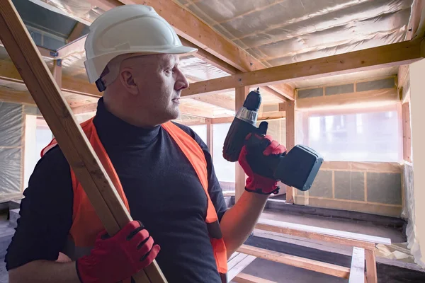 Repair work. Worker with electric screwdriver in his hands. Repairman does wall covering. Worker repairs the room. Walls of room are covered with insulation. Work with insulation from insid