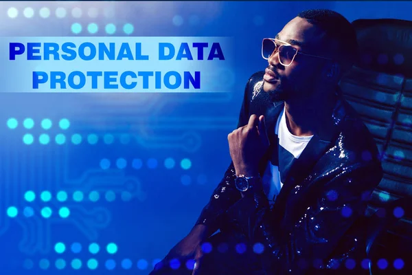 Personal data protection. A dark-skinned man is sitting in a chair on a blue background. The person next to the label about personal data protection. Business, technology, internet and network concept