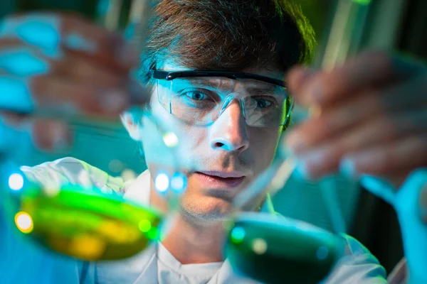 Close-up of laboratory assistant face next to test tubes. Laboratory assistant holds test tubes with multi-colored liquids. Career as a laboratory worker. chemist examines reagents. Chemist career