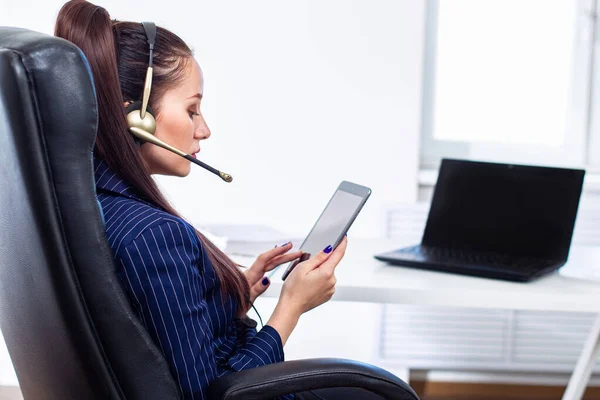 Businesswoman work from home. Home Office. Woman work from her home. Businesswoman in a leather chair. Woman in headphone for negotiations. Laptop next to a business woman. Girl in business suit.