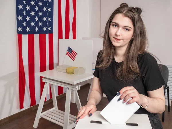 Voting in the US Presidential election. A young American woman at a polling station. The girl puts the ballot in the ballot box. Elections of the us President in 2020. USA election.