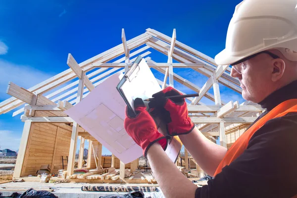 Builder construction. Man builder holds a clipboard in his hands. Architect on background house under construction. Building house made of wood. Architect edits room plans. Builder corrects drawings