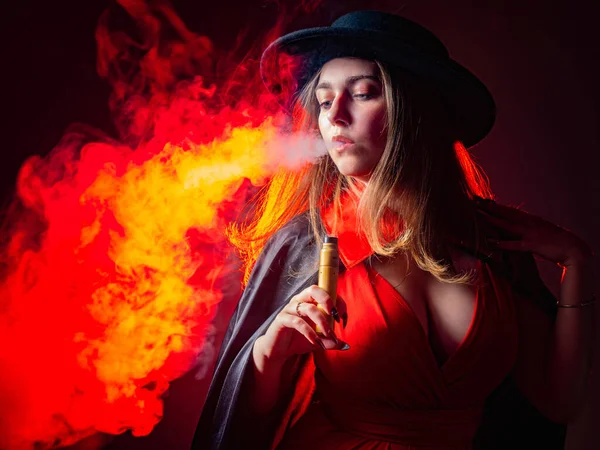 A woman smokes a VAPE. The girl lets out a stream of smoke from an electronic cigarette. A femme fatale with a VAPE in her hands. The concept of vaping. VAPE shop. Smoking electronic cigarettes.