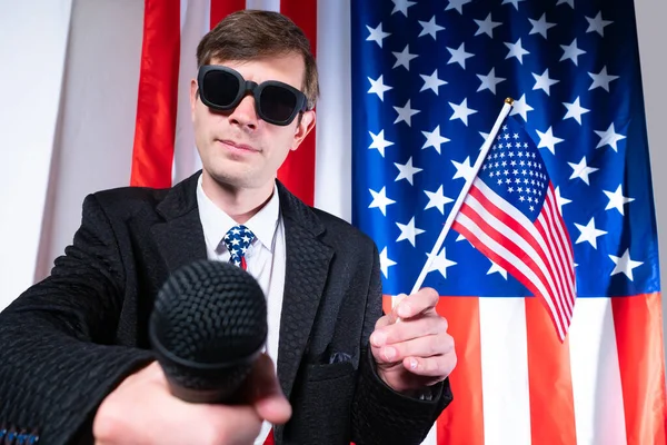 Report on the election of the President of the United States of America. Election debates in the United States. A reporter in black glasses holds out a microphone. A politician and US flags.