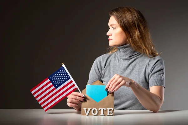 Election of the USA President. An American woman reflects on her choice when voting. A girl with an American flag and a ballot paper in her hands. Election of the American President.