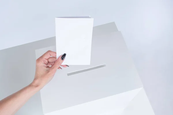 A woman hand drops a ballot into the ballot box. The concept of voting in elections in white. A woman takes part in elections.