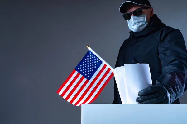 Violations in the US Presidential election. A man in black glasses and rubber gloves puts a stack of ballots in the ballot box. Election fraud. Illegal voting by an American in black clothing.