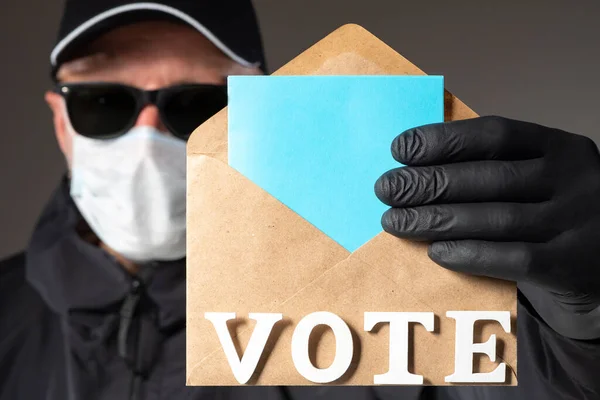 A man votes in an election wearing a protective mask and gloves. A person takes part in elections despite the epidemic. A man wearing rubber gloves and a mask holds a ballot paper.