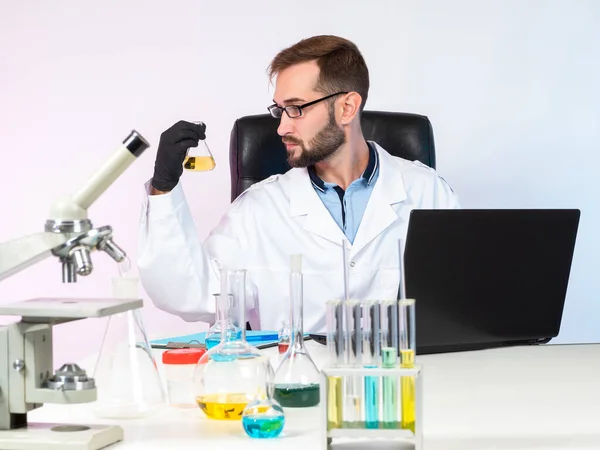 Chemical experiment. Research in the field of chemistry. The scientist examines the chemical liquid in the flask. Work in a chemical laboratory. Researcher in a white coat in the laboratory.