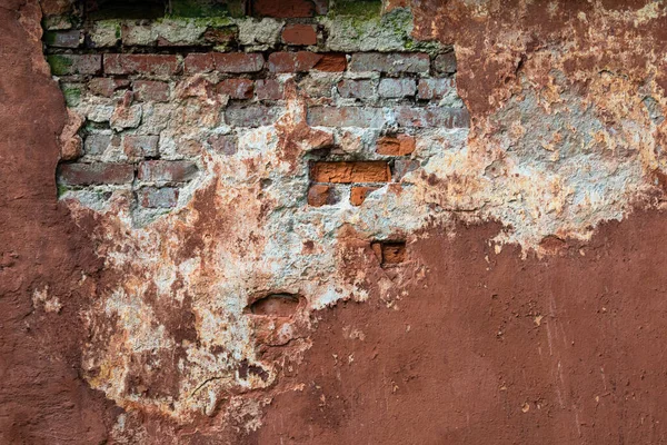 Old brown wall. Background walls with partially fallen off plaster. Background from the facade of an old house. Vintage construction background. A crumbling wall with bricks. Moss on old masonry.