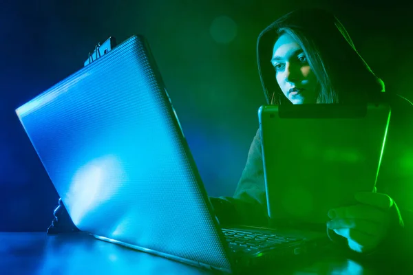 Freelancer girl at work. Girl next to laptop, tablet and smartphone. A young woman is doing urgent work. A woman with computer gadgets on a dark background.
