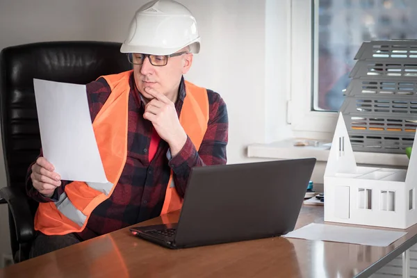 Work in a construction company. Work on the project of a new house. The engineer studies the document in his office. Workplace of the architect with a layout of the future cottage.