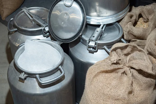Aluminum tank next to sacks of burlap. Tanks and bags in a warehouse close-up. Concept is a sweet farm. Sacks of grain in a farm warehouse. White foam in an aluminum tank. Milk storage tank