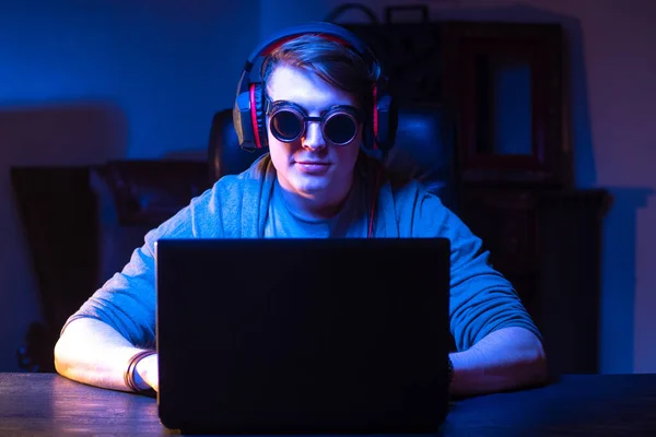 Guy in the headphones and sunglasses. Man in headphones plays games. Concept - video games on a laptop. Studen listens to music. Recreation. Concept - selling headphones. Gambling addiction.