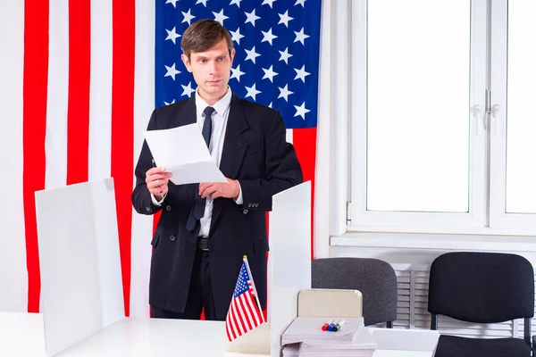 Voting in America. Presidential election in US. Man in business suit at polling station. America. Man with electoral bill on background of US flag. Human at presidential election USA. American Voter
