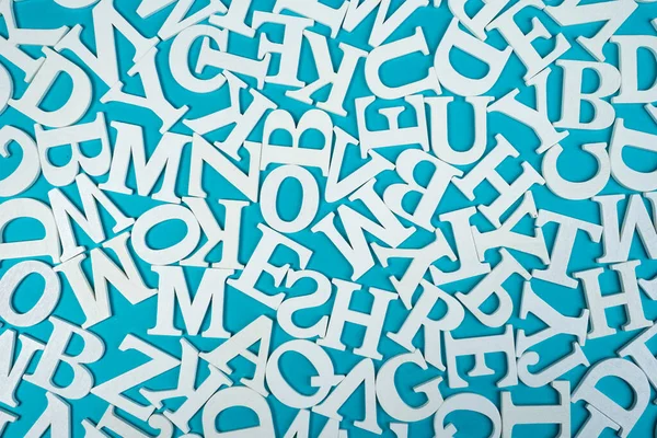 Background of white English letters on a blue background. A chaotic pattern of Latin characters. White letters of the Latin alphabet are on the table. The English alphabet.