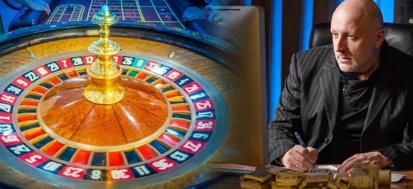 A man tries to develop a winning scheme in a casino. Secret winning formula. A man on a background of money and a roulette wheel. Casino. Cash game. Games of chance.