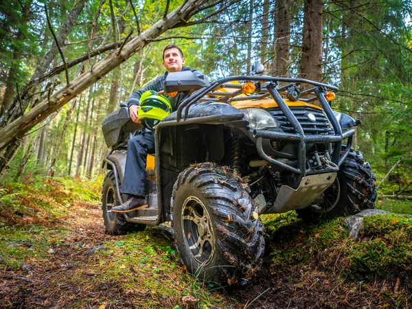 A man travels through the woods on the ATV. A man sits on the ATV in the forest. Off-road. A man travels on a quad.