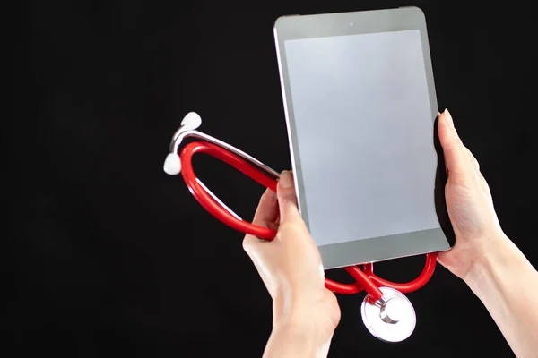Medical information. Medical reference system. Medical data. Hands with a tablet and a stethoscope close-up. Phonendoscope and tablet on a black background.