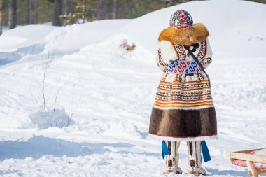 Russkinskaya, Rusya - 24 Mart 2018: Ulusal kuzey kıyafetleri içinde stoklu kadın karda tek başına durup kış ormanına bakıyor. Reindeer çobanTatil.