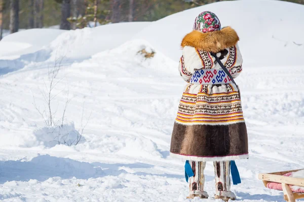 Russkinskaïa, Russie - 24 mars 2018 : Femme stagnante en vêtements nationaux nordiques debout seule sur la neige et regardant vers la forêt d'hiver. Vacances de l'éleveur de rennes . — Photo