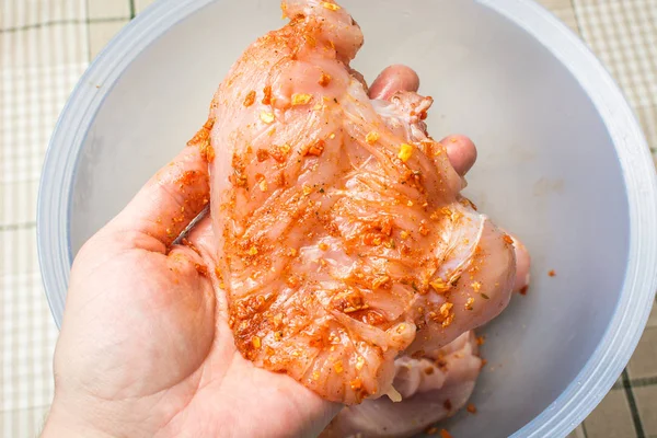 Raw chicken rubbed with spicy spices in male hand over large plate. — Stock Photo, Image