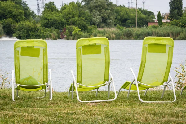 Three empty green lounge chairs for relaxing and sunbathing are standing on banks of river