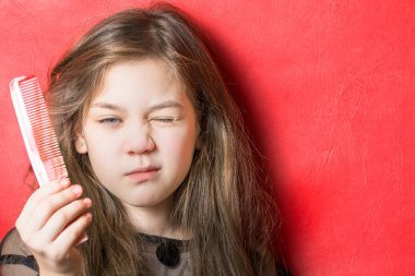 Güzel kız kırmızı bir arka plan üzerinde kapalı bir göz ile bir tarak gösterir