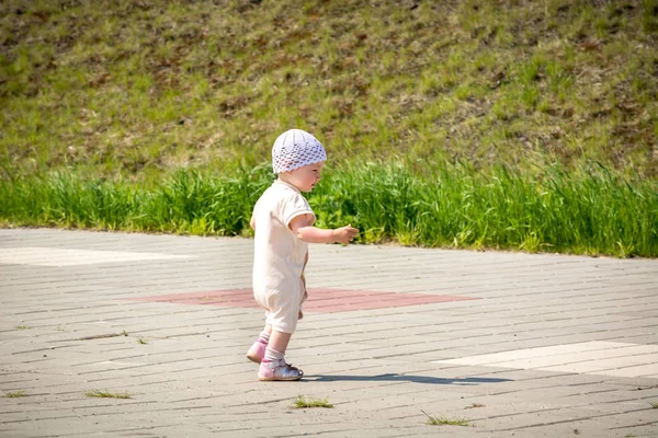 Маленький ребенок в белом костюме бегает по асфальтированной дорожке от набережной речного порта — стоковое фото