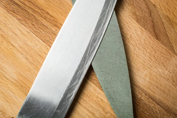 Тонкий кухонный нож для овощей с молотым камнем из грубого абразива на деревянной доске . — стоковое фото
