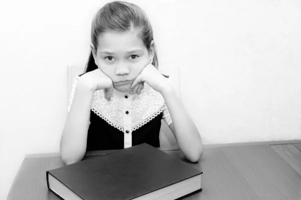 Vacker Schoolgirl sitter vid ett skrivbord och vill inte läsa boken — Stockfoto