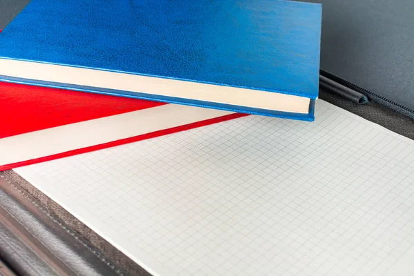 Синяя и красная книги лежат на открытой черной кожаной папке с ноутбуком — стоковое фото