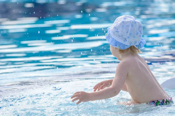 Şapkalı küçük çocuk mavi havuzda dalgalar dağıtır. — Stok fotoğraf