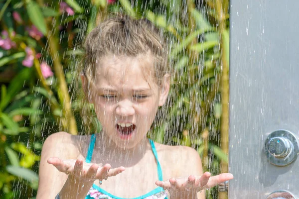 Маленька дівчинка, що стоїть під душем на пляжі, ловить руку на краплі води . — стокове фото