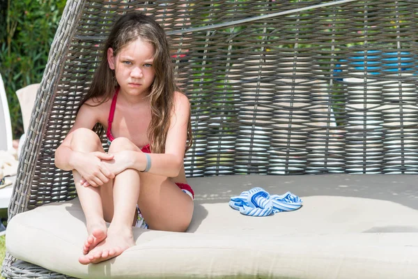 Chica triste en traje de baño sentado en una tumbona de mimbre escondida del sol . — Foto de Stock