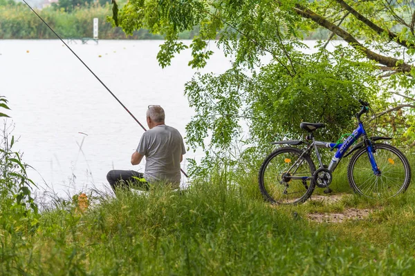 KRASNODAR, RUSSIE - 7 JUIN 2018 : Un pêcheur âgé capture du poisson dans le lac à partir du rivage . — Photo