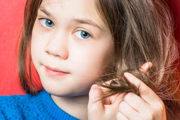 Cute little girl in blue blouse reels her hair on a red background — Stock Photo, Image