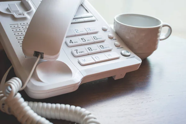 Pegou o telefone em um número de escritório com uma caneca vazia do chá na mesa de madeira . — Fotografia de Stock