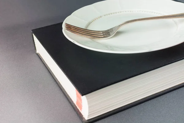 Kalın siyah bir kitabın üzerinde çatallı beyaz tabak var. — Stok fotoğraf